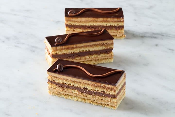 Slice of Porto's Opera Cake with chocolate glaze and a coffee bean on top